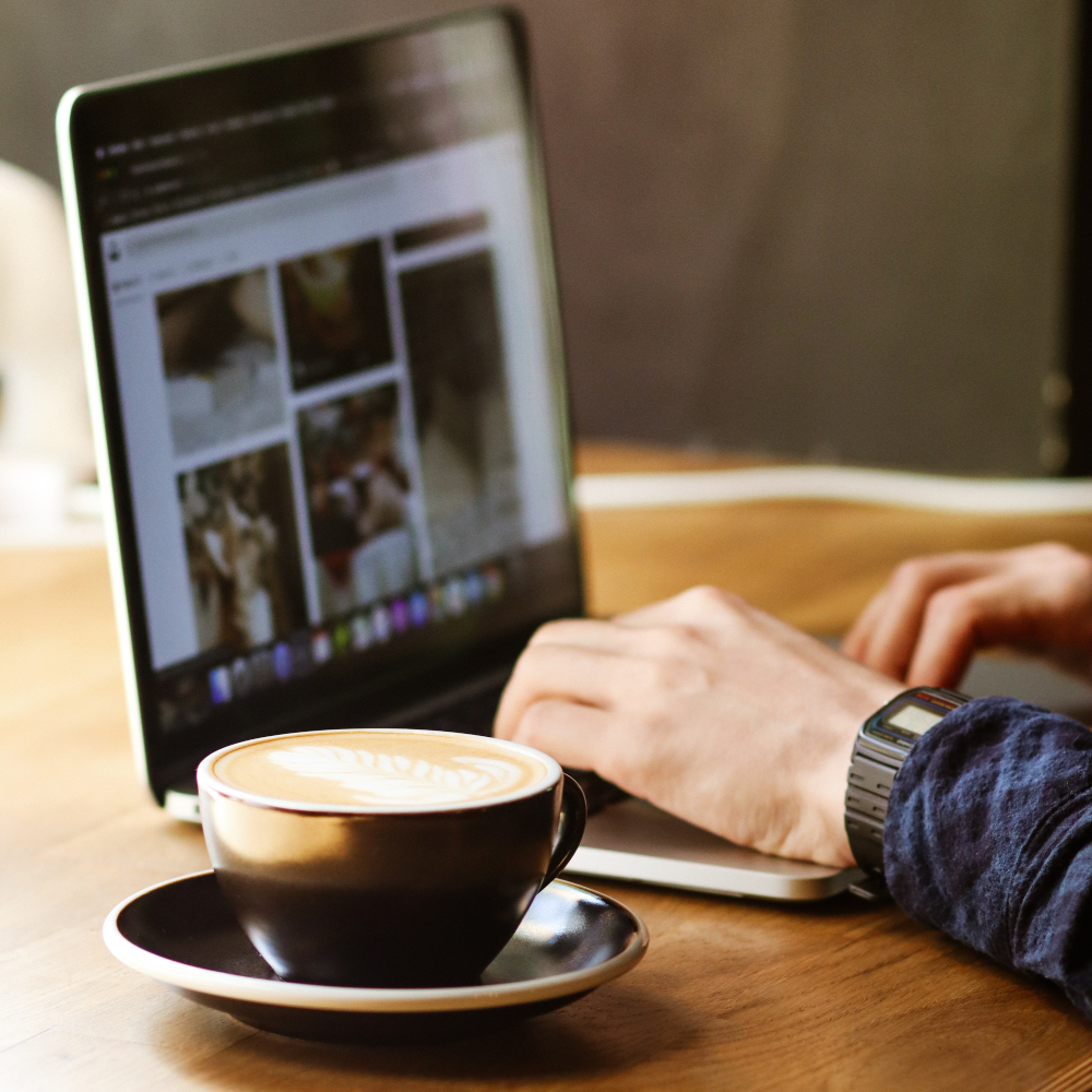 A person typing on a laptop with a latte beside it